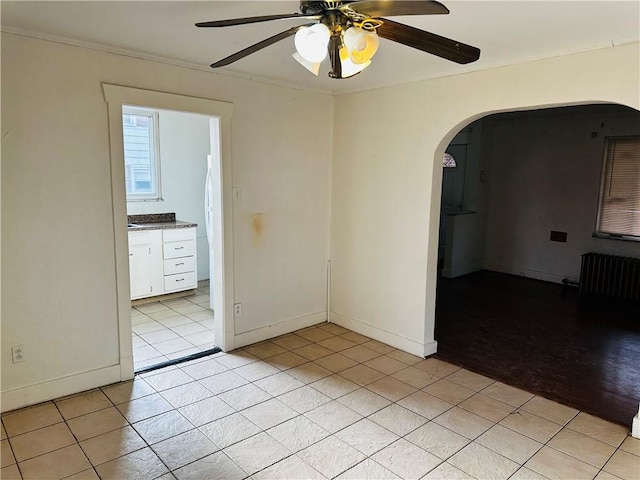 spare room with arched walkways, ceiling fan, radiator heating unit, light tile patterned floors, and baseboards