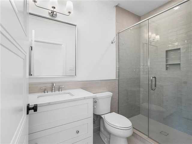 bathroom featuring a shower stall, vanity, toilet, wainscoting, and tile walls