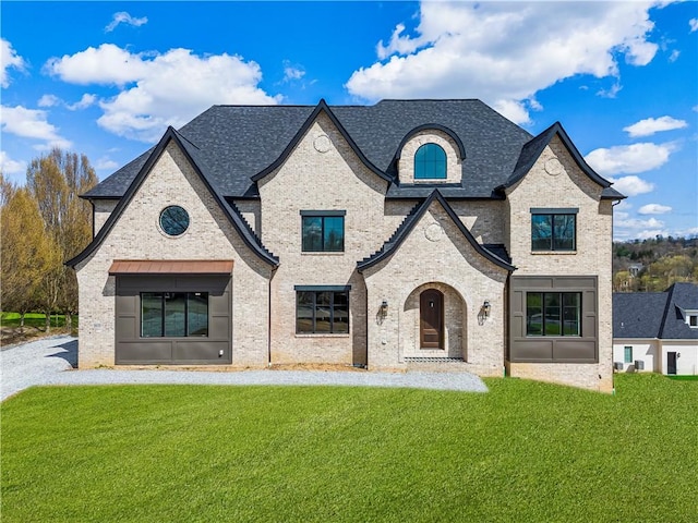 french country style house with a front yard, a shingled roof, and brick siding