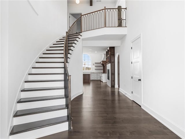 staircase featuring wood finished floors, arched walkways, a high ceiling, and baseboards