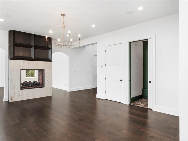 unfurnished living room with a chandelier, dark wood-style floors, arched walkways, baseboards, and recessed lighting