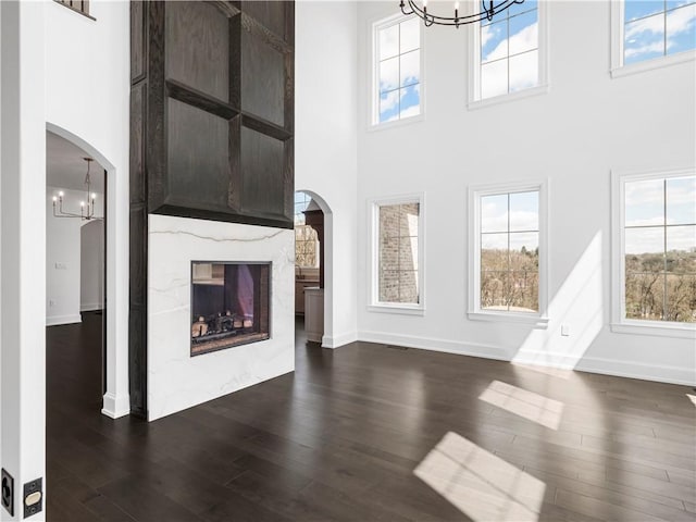 unfurnished living room with arched walkways, a chandelier, a high ceiling, and a high end fireplace