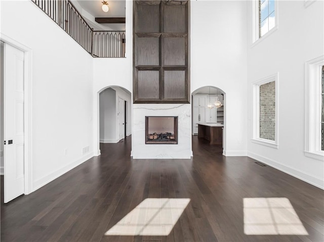 unfurnished living room with arched walkways, a high ceiling, wood finished floors, baseboards, and a chandelier