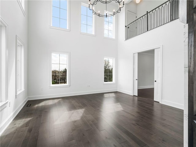 unfurnished living room featuring a high ceiling, dark wood-type flooring, healthy amount of natural light, and a chandelier