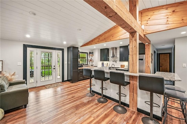 kitchen with a kitchen breakfast bar, wall chimney range hood, light wood finished floors, recessed lighting, and light stone countertops