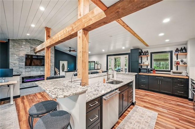 kitchen with a sink, stainless steel dishwasher, open floor plan, light wood-type flooring, and lofted ceiling