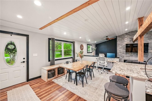 dining room featuring light wood finished floors, a desk, lofted ceiling, a ceiling fan, and a fireplace