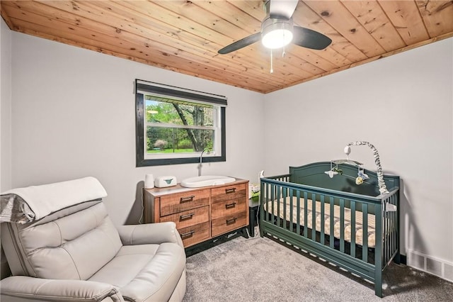 carpeted bedroom featuring wood ceiling, ceiling fan, a nursery area, and baseboards