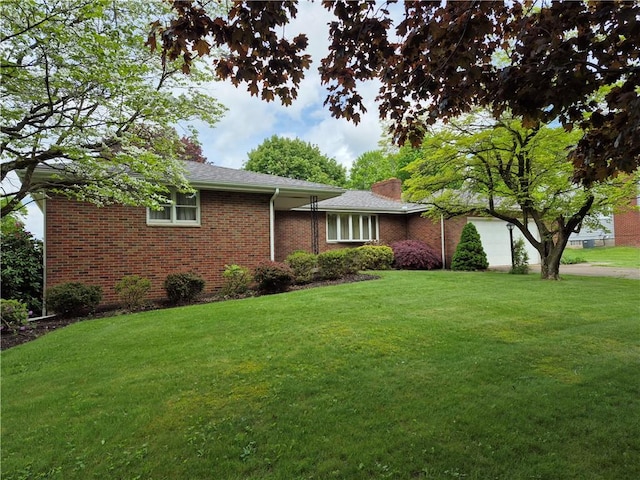 view of front of house with an attached garage, a front yard, brick siding, and a chimney