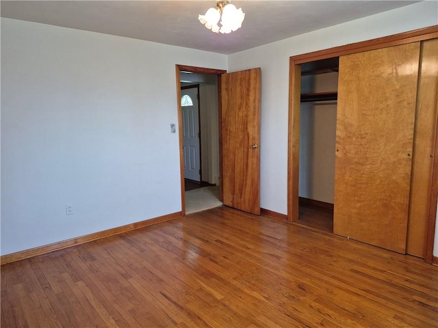 unfurnished bedroom with hardwood / wood-style flooring, a closet, baseboards, and a chandelier