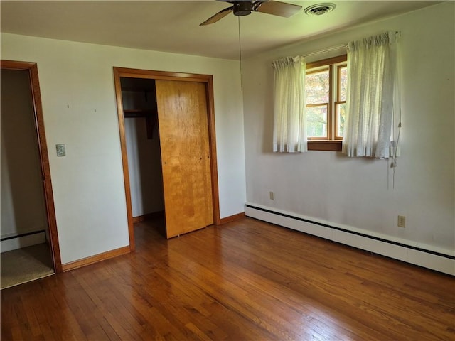 unfurnished bedroom featuring a baseboard heating unit, wood-type flooring, a closet, baseboards, and a ceiling fan