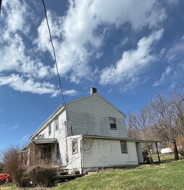 rear view of property featuring a lawn and a chimney