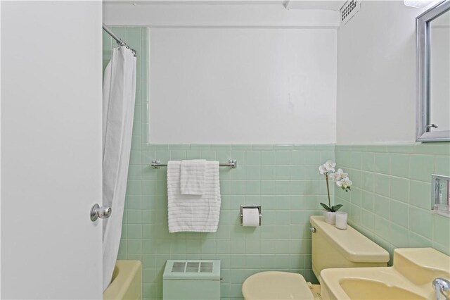 bathroom featuring tile walls, toilet, a sink, and wainscoting
