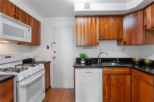 kitchen featuring white appliances, a sink, light wood-type flooring, brown cabinetry, and dark stone counters