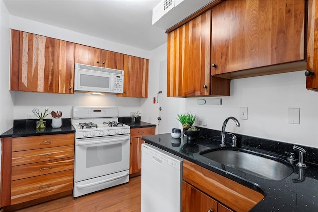 kitchen with white appliances, brown cabinetry, light wood-style floors, a sink, and dark stone countertops