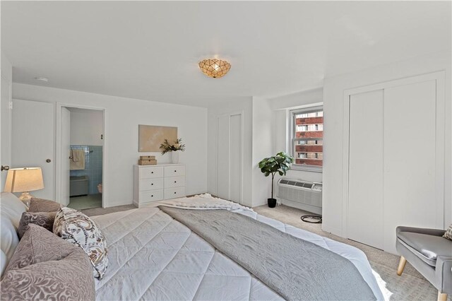 bedroom with carpet flooring, multiple closets, a wall unit AC, and ensuite bath