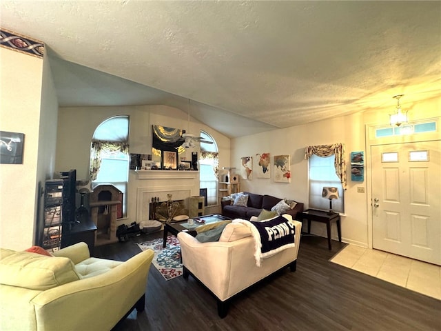 living room with a fireplace, wood finished floors, a textured ceiling, lofted ceiling, and baseboards