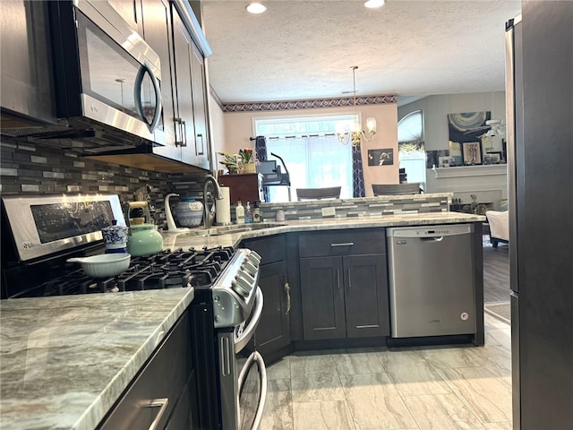kitchen featuring stainless steel appliances, a peninsula, backsplash, a textured ceiling, and a chandelier
