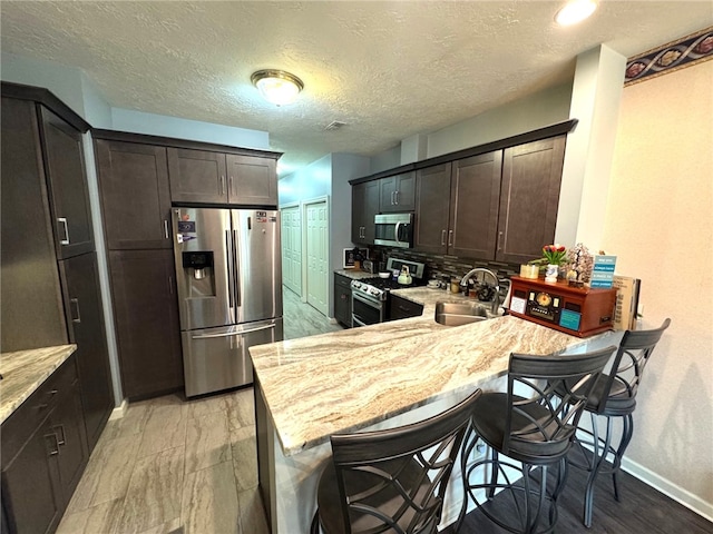 kitchen featuring appliances with stainless steel finishes, a sink, baseboards, and dark brown cabinets