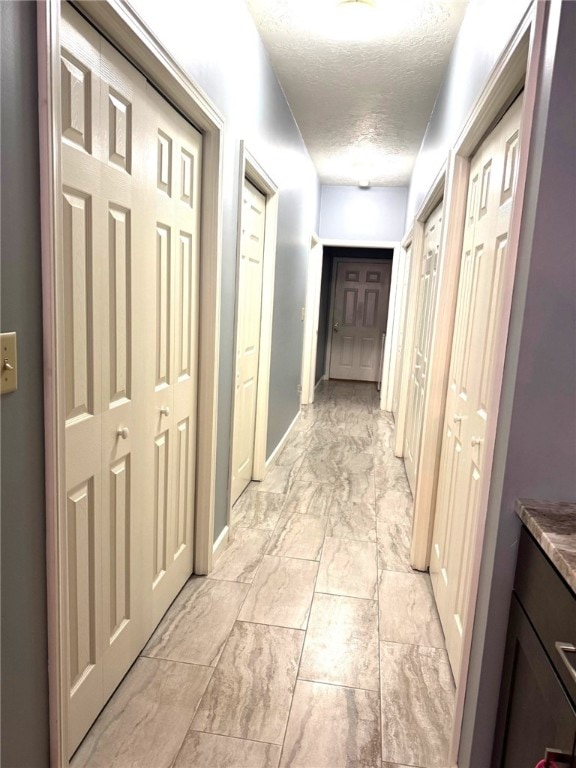 corridor with light marble finish floors, a textured ceiling, and baseboards