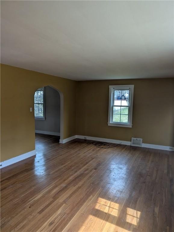 spare room featuring arched walkways, healthy amount of natural light, wood finished floors, and baseboards