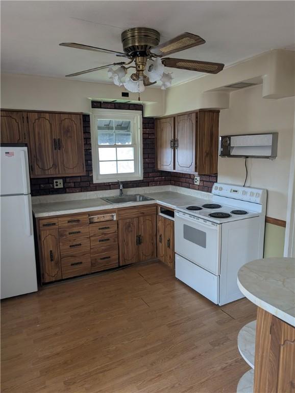 kitchen with white appliances, a sink, tasteful backsplash, light countertops, and light wood finished floors