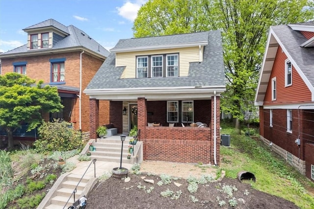 bungalow-style house featuring covered porch, central AC unit, brick siding, and a shingled roof