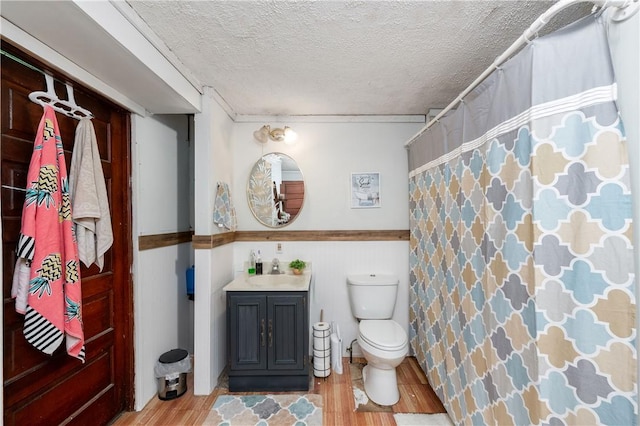 bathroom with wood finished floors, a textured ceiling, toilet, vanity, and a shower with curtain