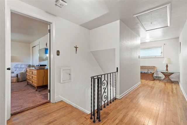hall featuring an upstairs landing, light wood-style floors, attic access, and baseboards