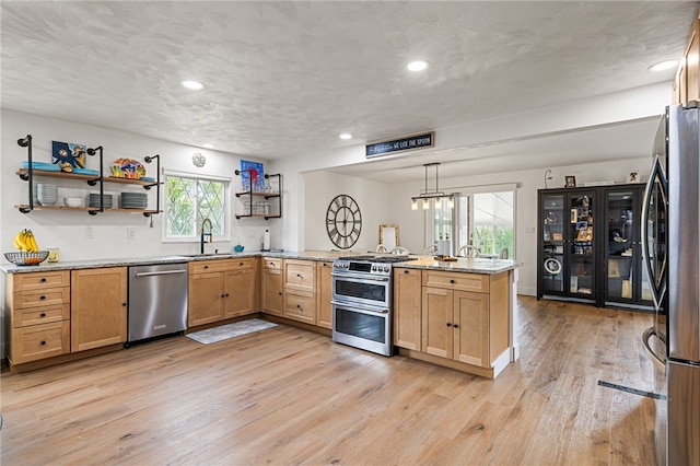 kitchen featuring appliances with stainless steel finishes, a peninsula, a sink, light wood-style floors, and light stone counters