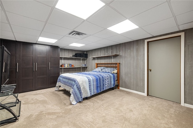 bedroom with light colored carpet, a paneled ceiling, baseboards, and wooden walls