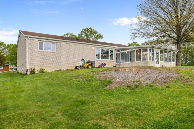 back of property with a sunroom, brick siding, and a yard