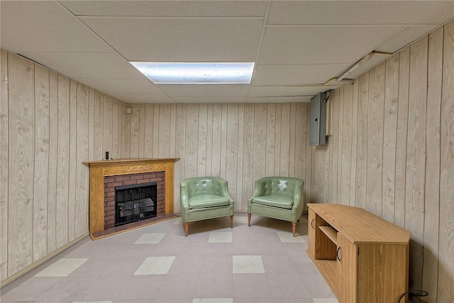 living area featuring a paneled ceiling, light floors, wooden walls, and a brick fireplace