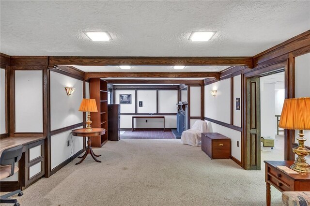sitting room with carpet floors, a textured ceiling, beamed ceiling, baseboards, and a desk