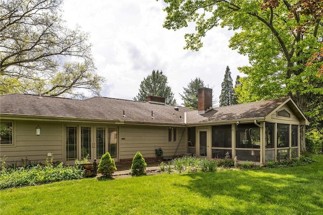 rear view of property with a chimney, a sunroom, and a yard