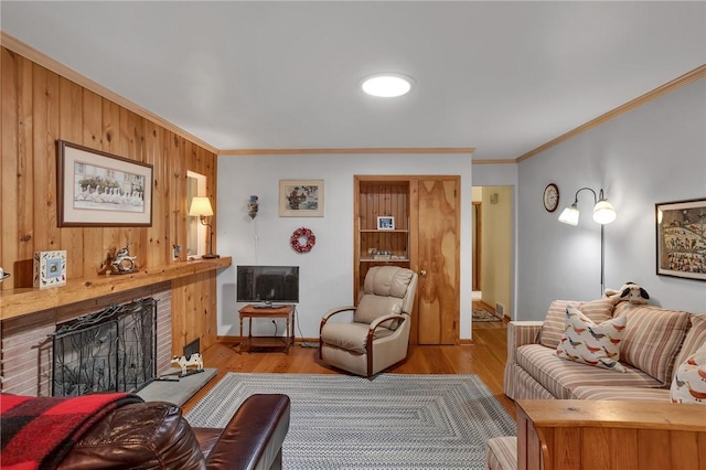 living area with ornamental molding, a fireplace with raised hearth, wood finished floors, baseboards, and wood walls