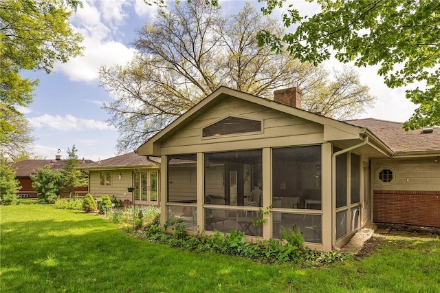 rear view of property with a chimney, a sunroom, and a yard
