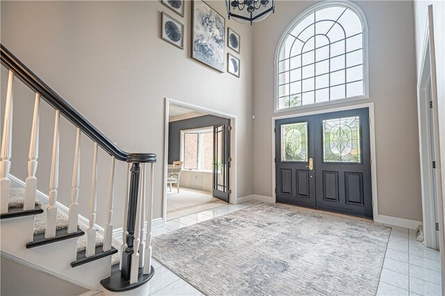 tiled entrance foyer featuring a high ceiling, stairs, and baseboards