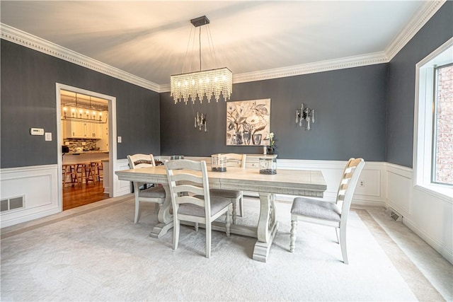 dining area with a chandelier, ornamental molding, carpet floors, a wainscoted wall, and a decorative wall