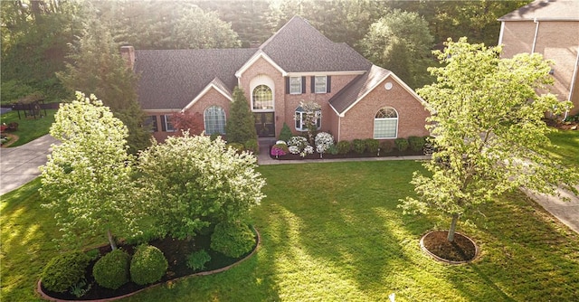 view of front of home with brick siding, a front lawn, and a shingled roof