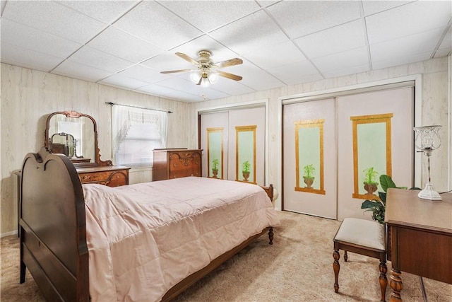 bedroom with carpet flooring, two closets, a drop ceiling, and a ceiling fan