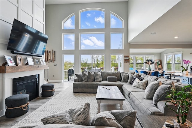living room featuring light wood-style floors, a towering ceiling, a glass covered fireplace, baseboards, and recessed lighting