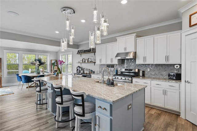 kitchen with stainless steel range with gas stovetop, under cabinet range hood, a sink, open shelves, and white cabinetry