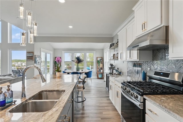 kitchen featuring stainless steel range with gas stovetop, a sink, under cabinet range hood, light stone counters, and recessed lighting