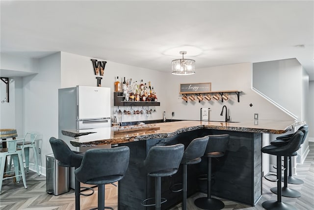 indoor wet bar with freestanding refrigerator, decorative light fixtures, and a chandelier