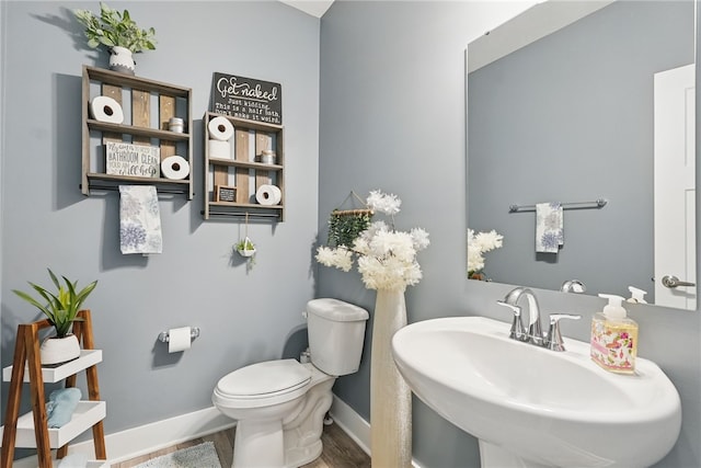 half bathroom with toilet, a sink, baseboards, and wood finished floors
