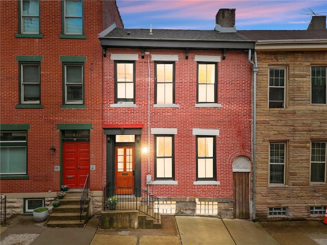 townhome / multi-family property with brick siding, a chimney, and a shingled roof