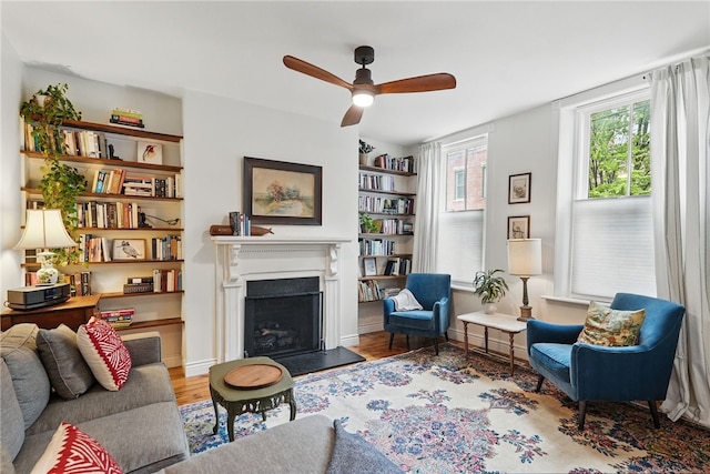 living area with a ceiling fan, wood finished floors, and a fireplace with raised hearth