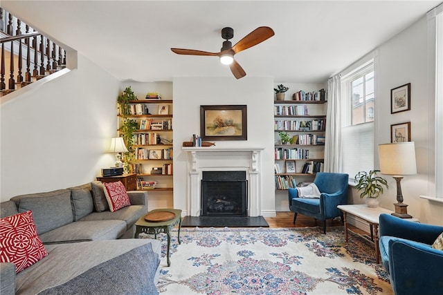 living area with ceiling fan, a fireplace, wood finished floors, and stairs