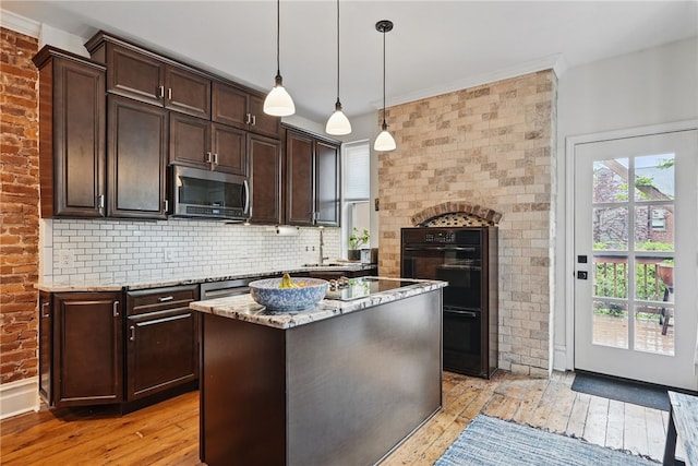kitchen with stainless steel microwave, light wood finished floors, dark brown cabinets, light stone countertops, and brick wall